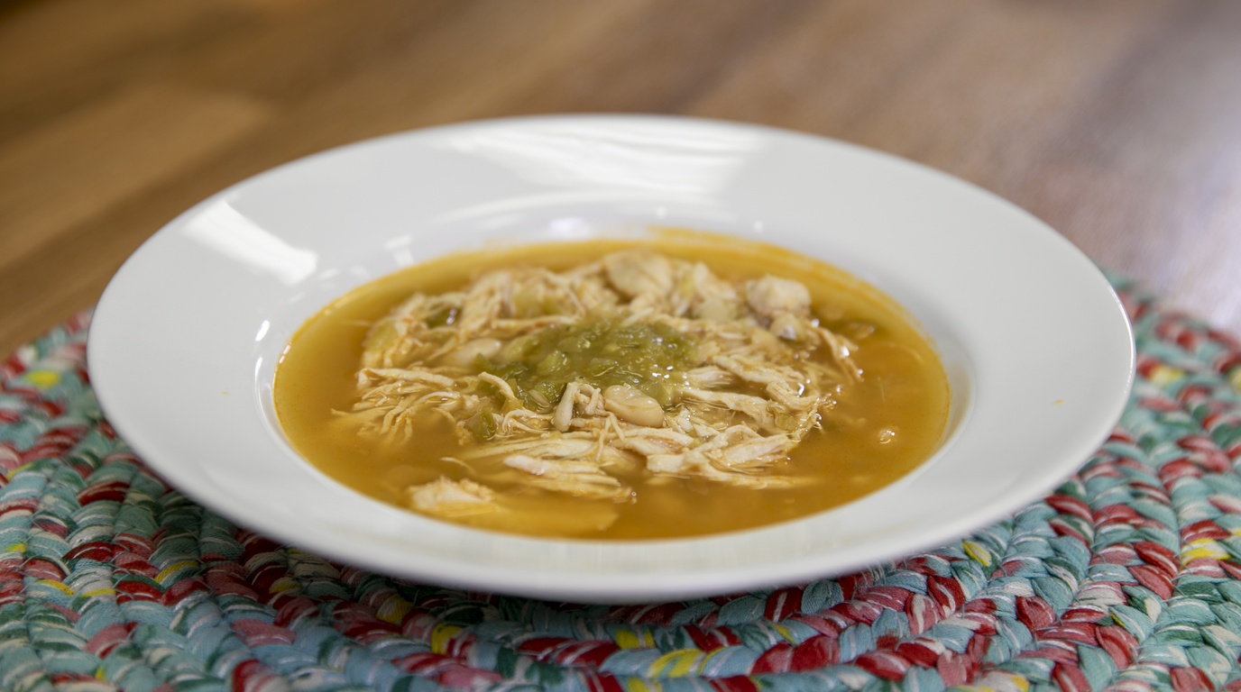 Macro close-up of simmering creamy white chicken chili with tender shredded chicken breasts, white cannellini beans, sweet corn, green chiles, and cream cheese