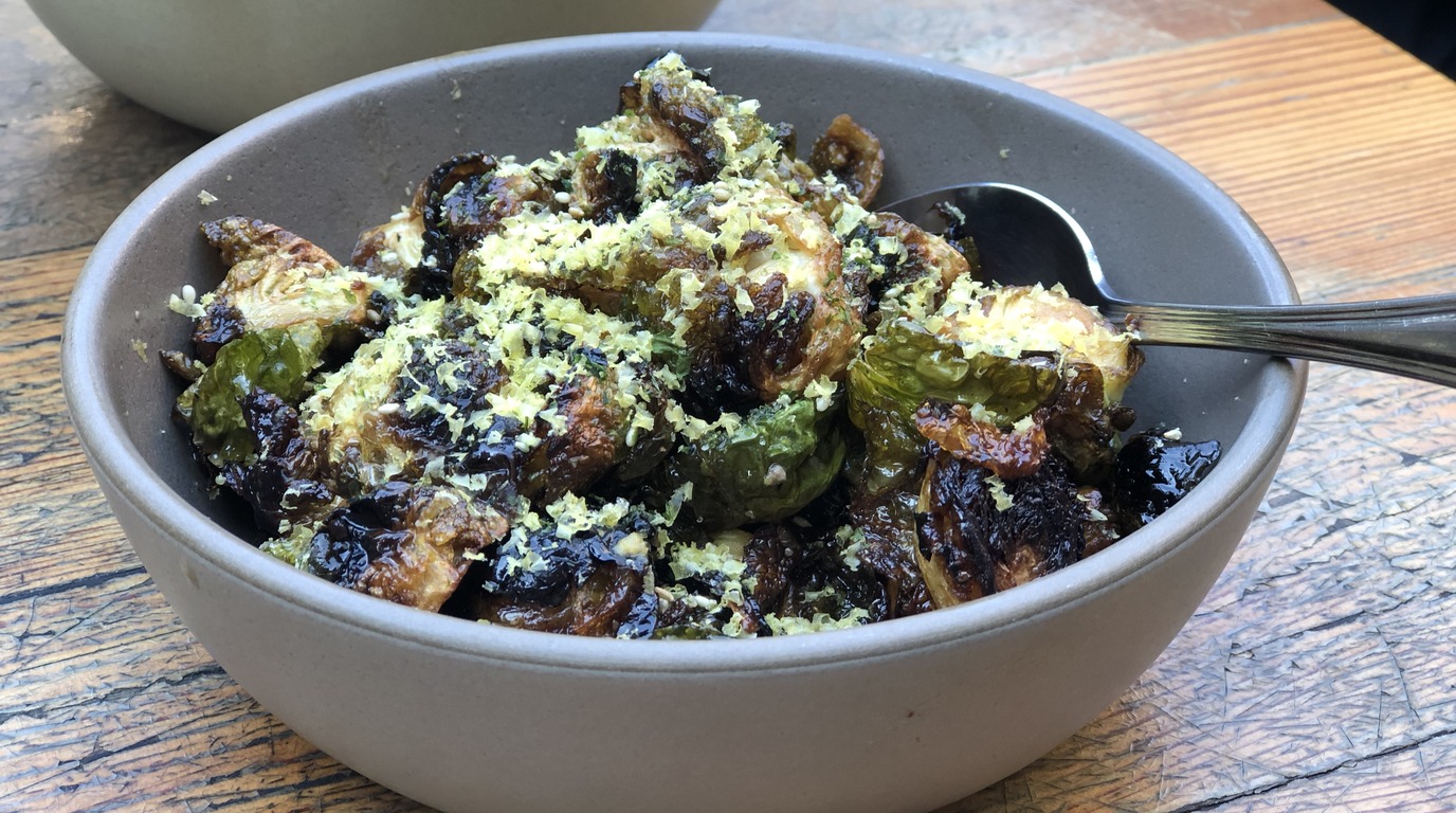 Macro close-up of golden crispy smashed brussels sprouts crusted with bubbly Parmesan cheese and fresh herbs