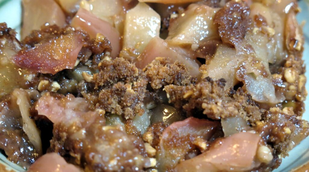 Ultra close-up macro view of golden crisp oat streusel topping with tender bubbling cinnamon spiced apples and warm salted caramel drizzle