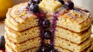 Ultra close-up macro shot of fluffy golden lemon ricotta pancakes with melting butter, fresh lemon zest, and dripping warm blueberry compote