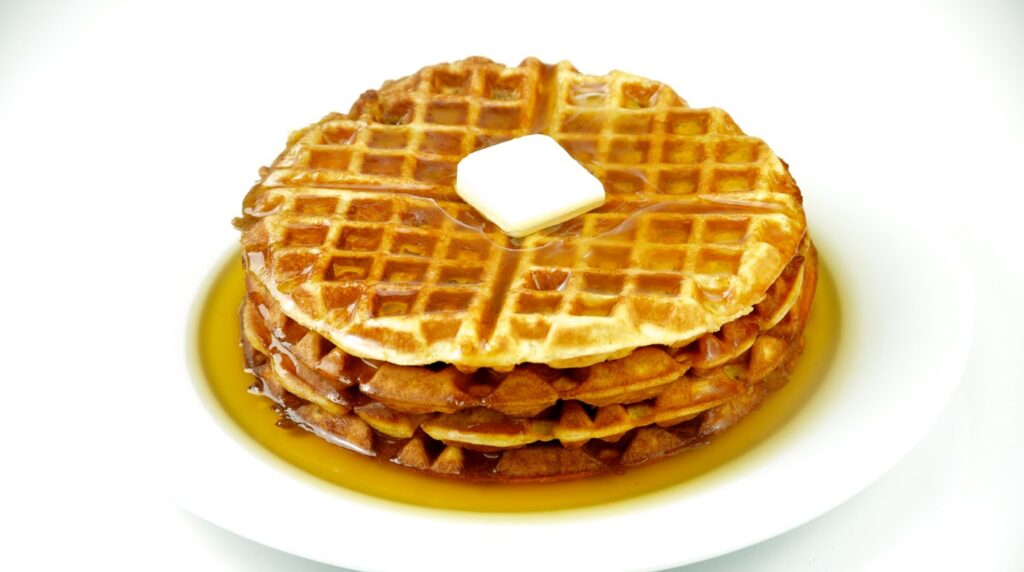 Ultra close-up macro view of golden crisp Belgian pumpkin waffle grid pockets filled with melting spiced butter and dripping pure maple syrup