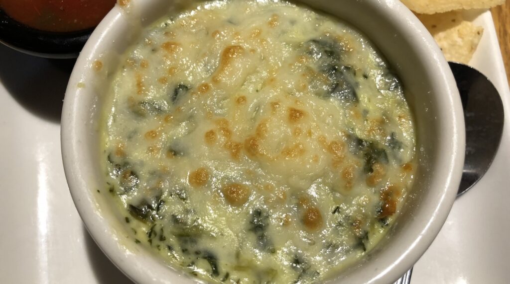 Ultra close-up macro view of hot bubbly spinach artichoke dip with melted golden browned mozzarella and parmesan cheese crust