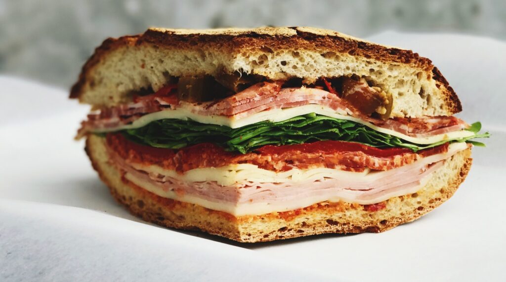 Macro close-up of a toasted Italian grinder salad sandwich packed with halal deli cuts, melted provolone cheese, and vibrant zesty chopped grinder salad